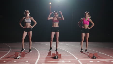 Three-women-athletes-prepare-for-a-track-race-in-a-dark-stadium-with-streetlights-on.-Time-lapse-footage-of-warm-up-and-concentration-of-a-group-of-women-before-the-race-on-the-track